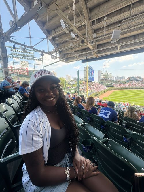Elisabeth Christina in shorts and baseball cap sitting in stands with baseball field in background