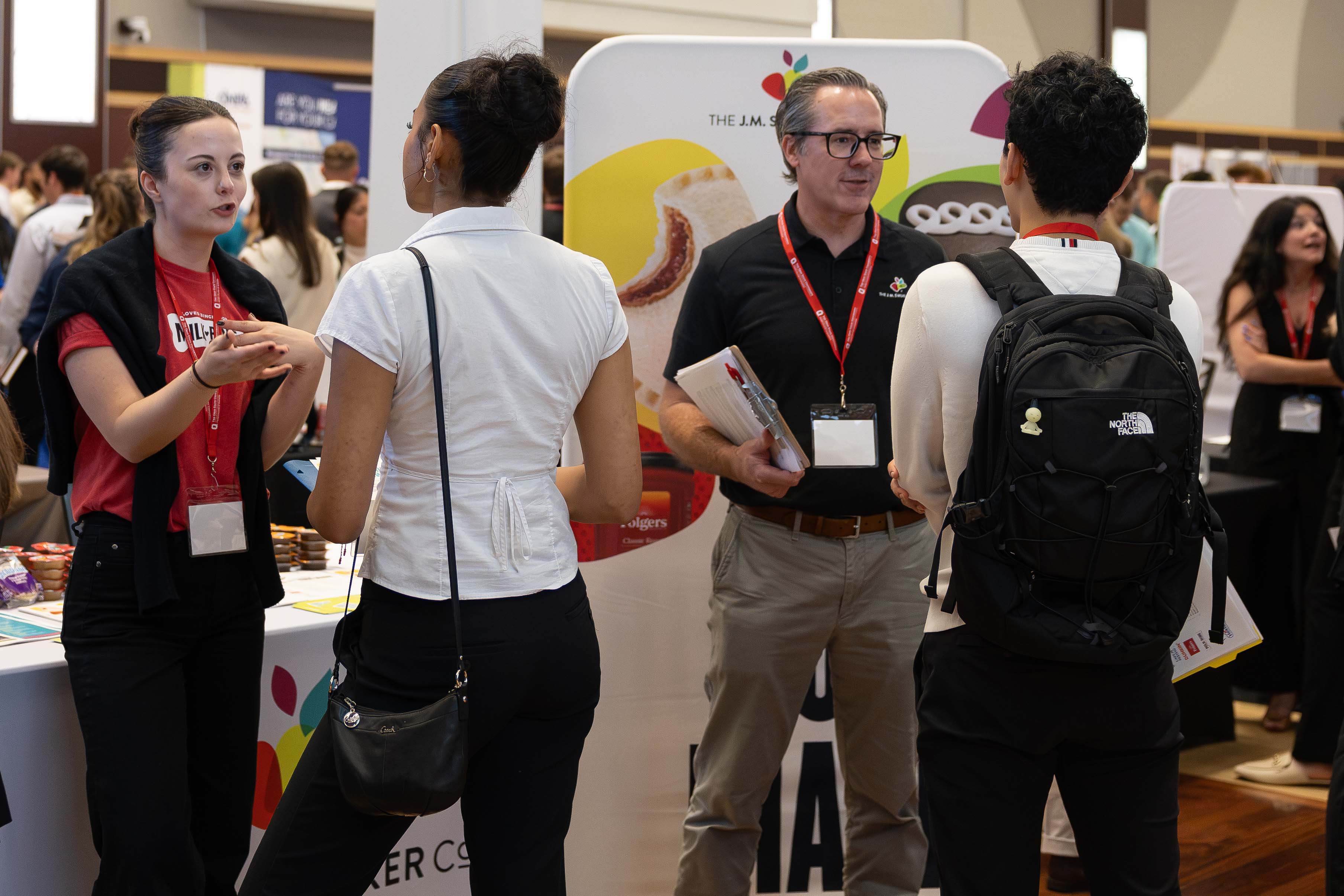 Two company recruiters stand in front of a display table talking to two students attending the career fair.