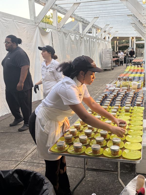 Woman in ballcap and apron sets mason jars on plates at a catering event