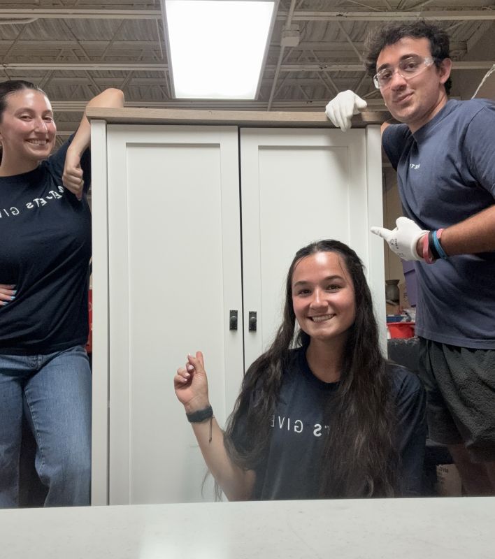 Three people pointing a cabinet.
