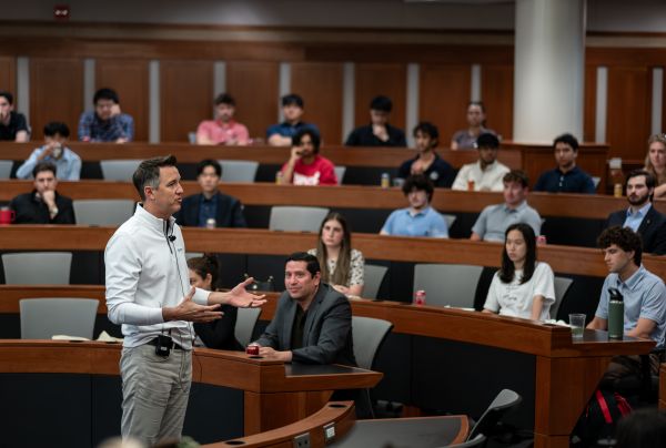 Man standing in center of lecture hall with arms raised out in front of him