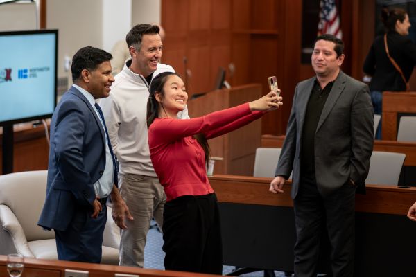Woman with cell phone outstretched in front of two men.