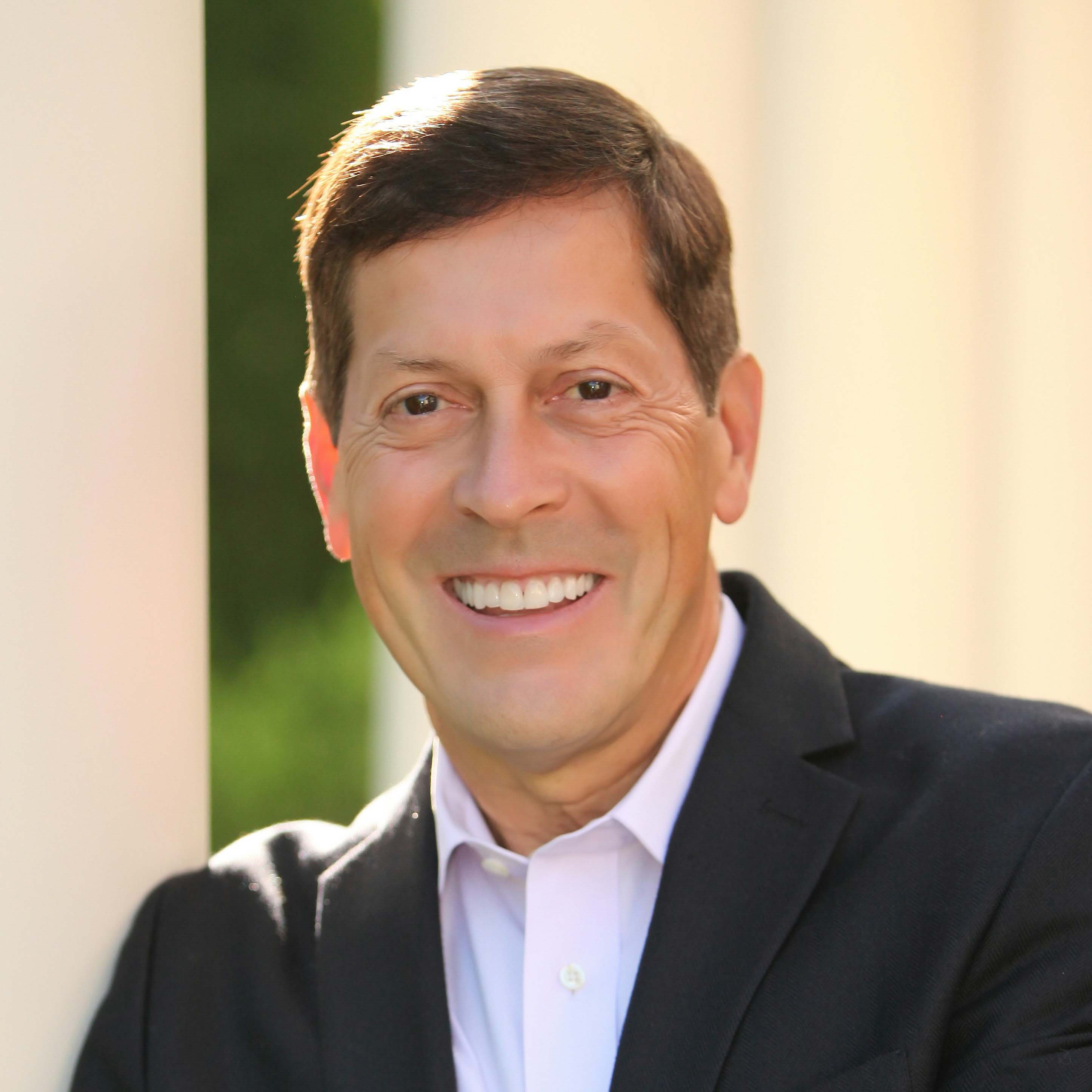 Headshot of Ric Dillon in a white collared shirt and dark blazer.