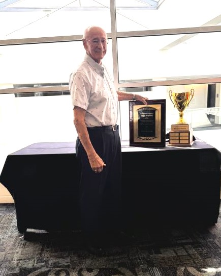 Man stands at draped table holding plaque next to trophy