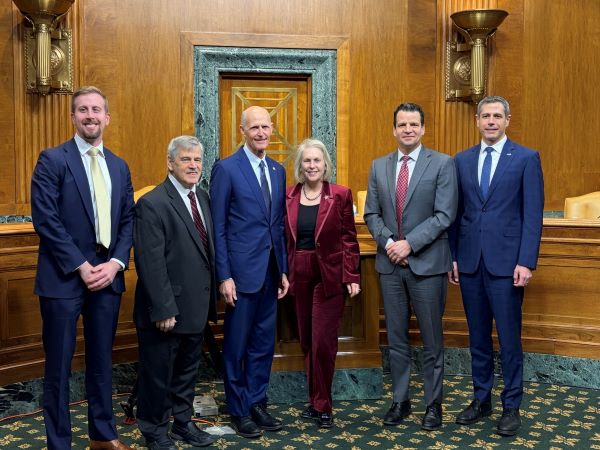 Four men, one woman in a suit pose in the Senate chambers