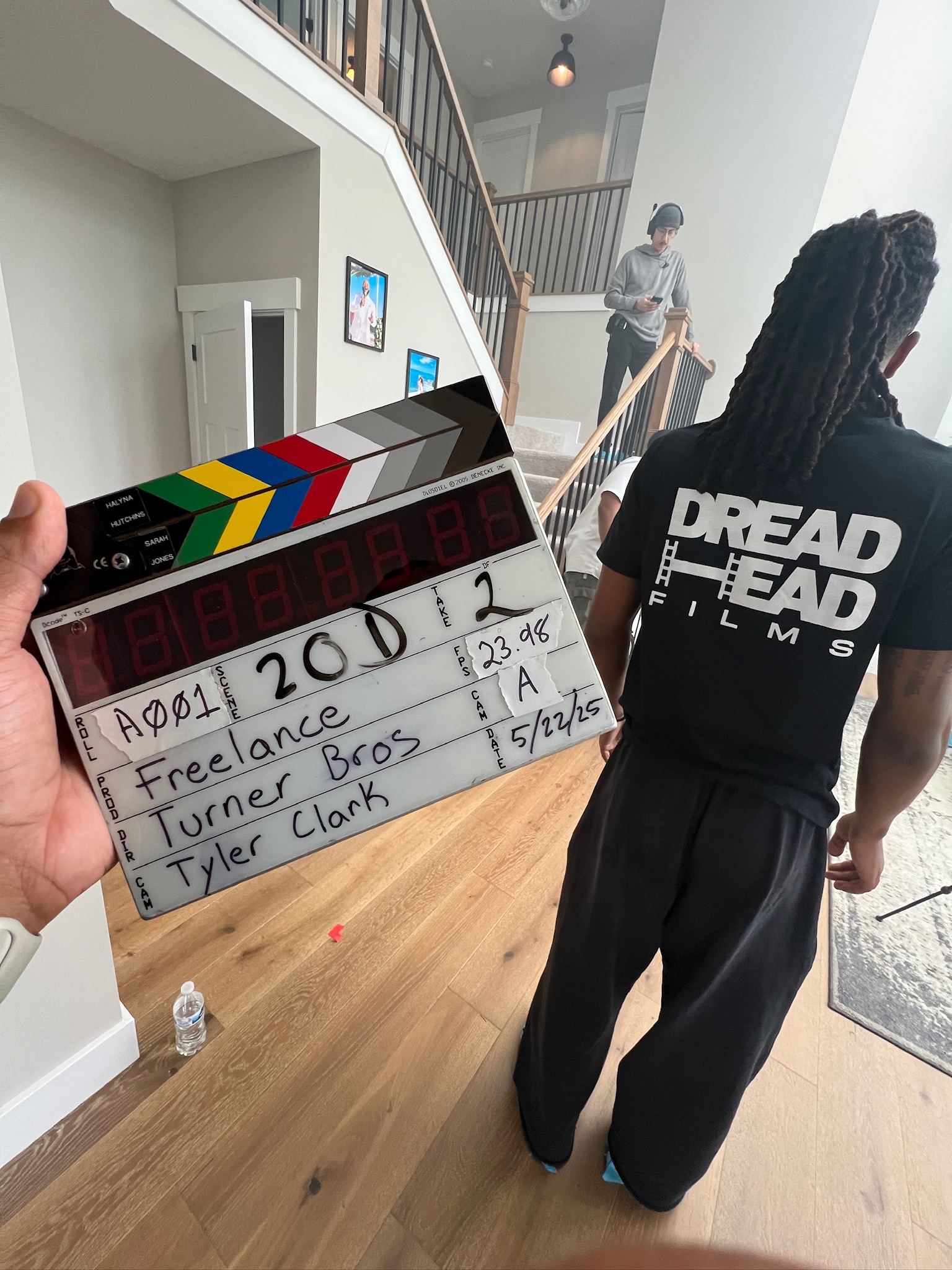 Hand holding a clapperboard with scene information in front of a scene in a house.
