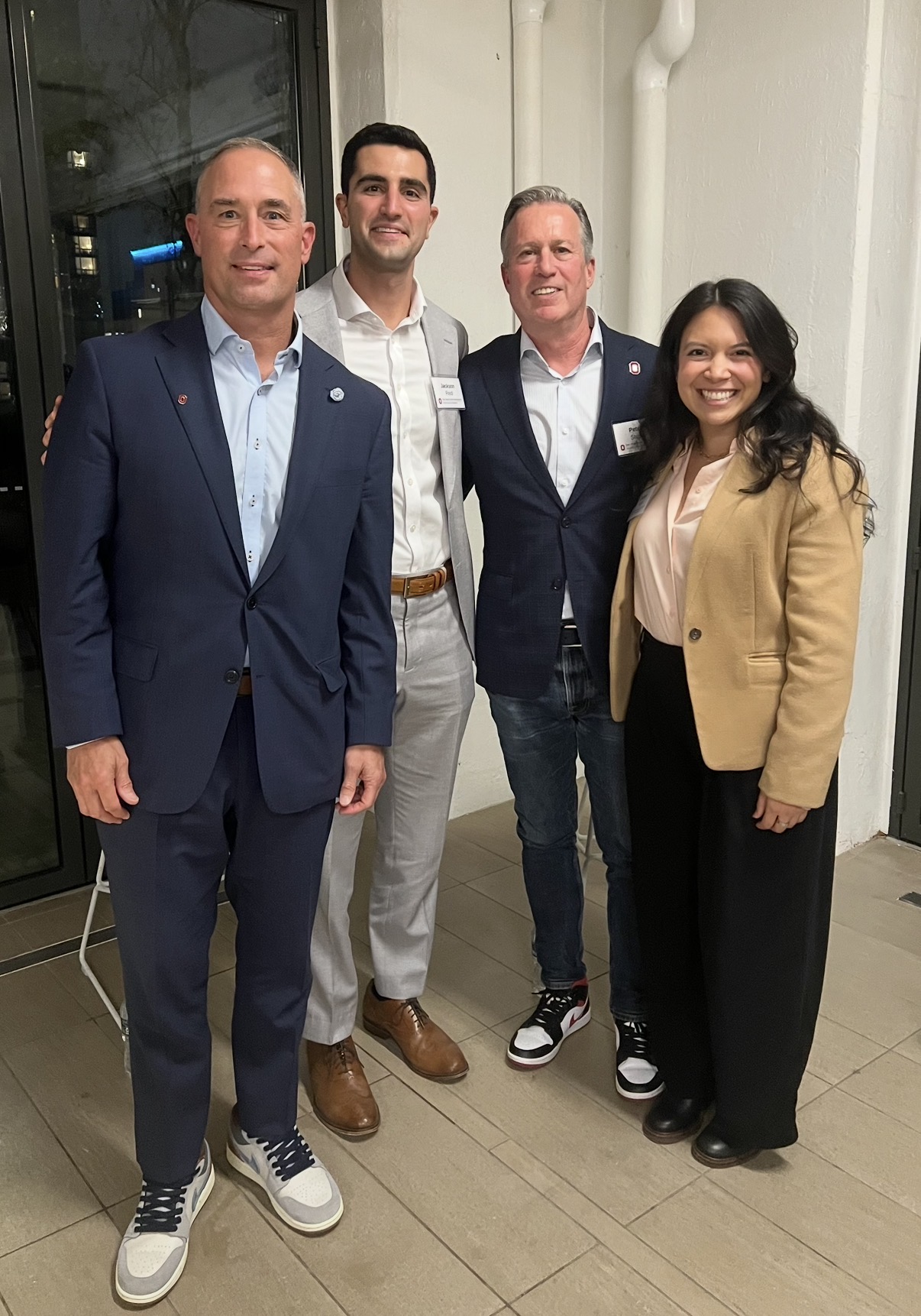 Sydney Roth, far right, is standing with three men who are Fisher alumni. They are all wearing suits and posing with their arms around one another.