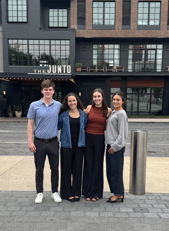 One man and three women, arm in arm, stand on the sidewalk outside a hotel in Columbus
