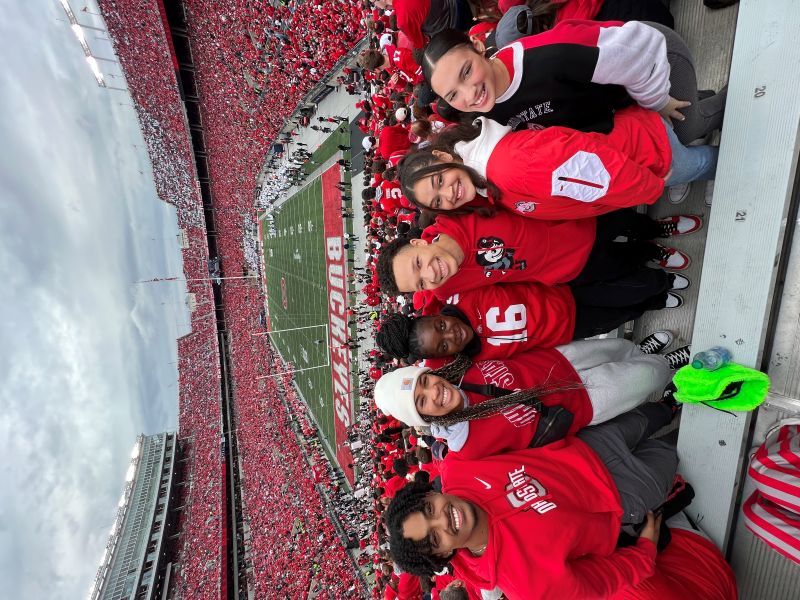 Group of students decked out in Ohio State gear withe the stadium and football field in background