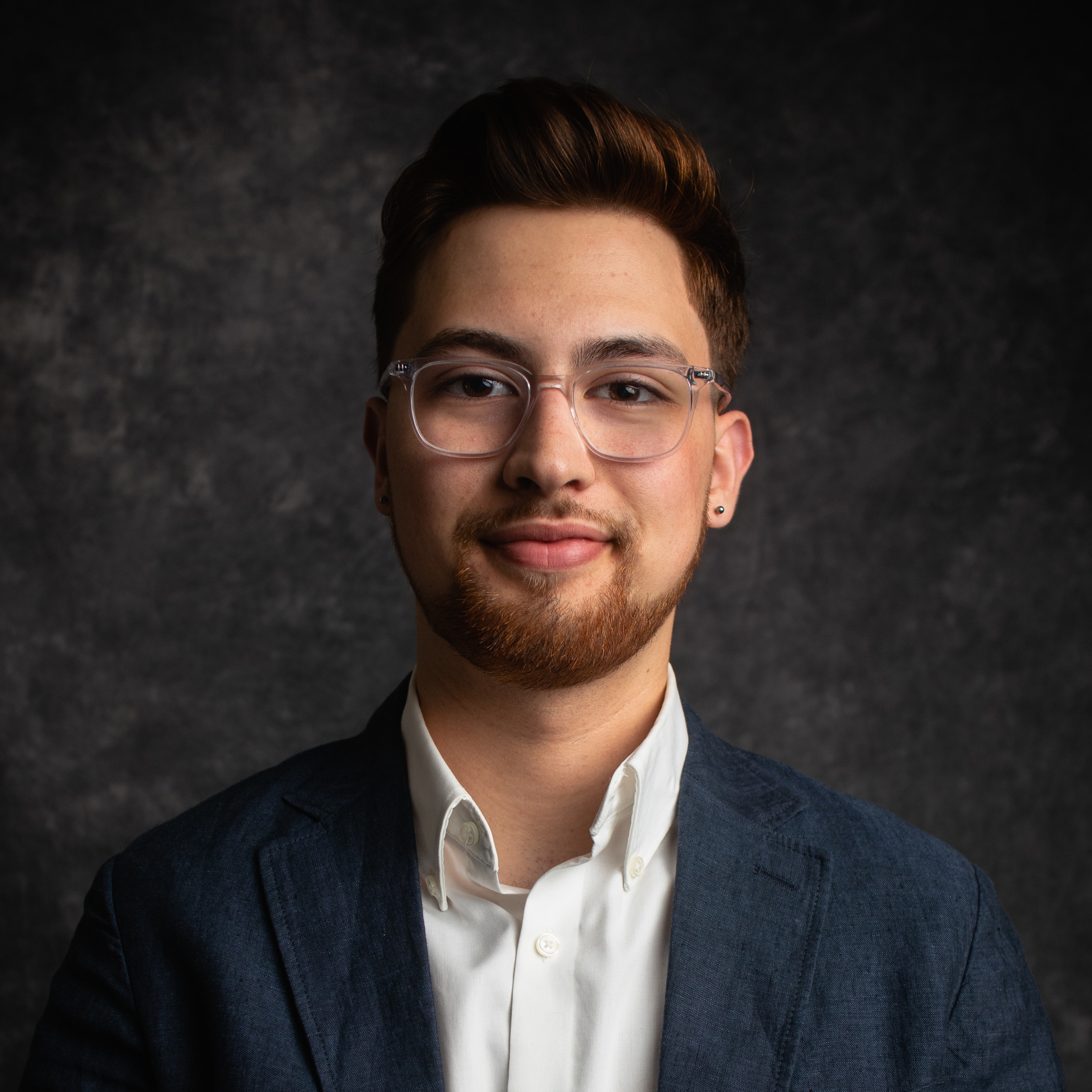 Headshot of Tobias Zuniga-Shaw wearing a white shirt and dark blazer.