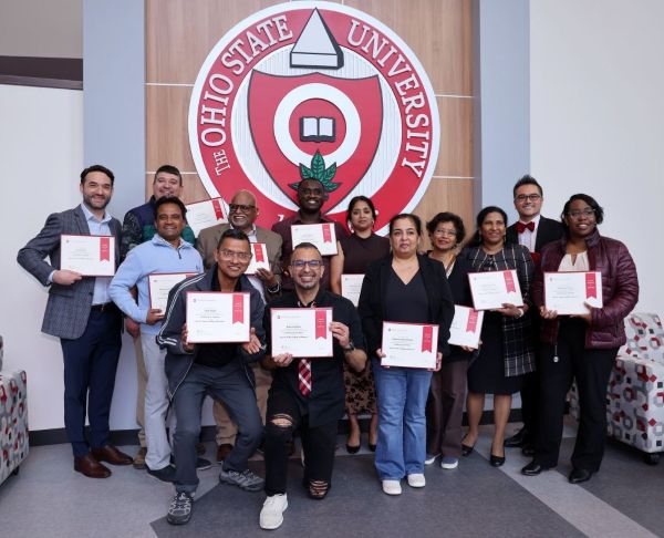 Group of individuals in business attire hold certificates in from of the Ohio State University seal.