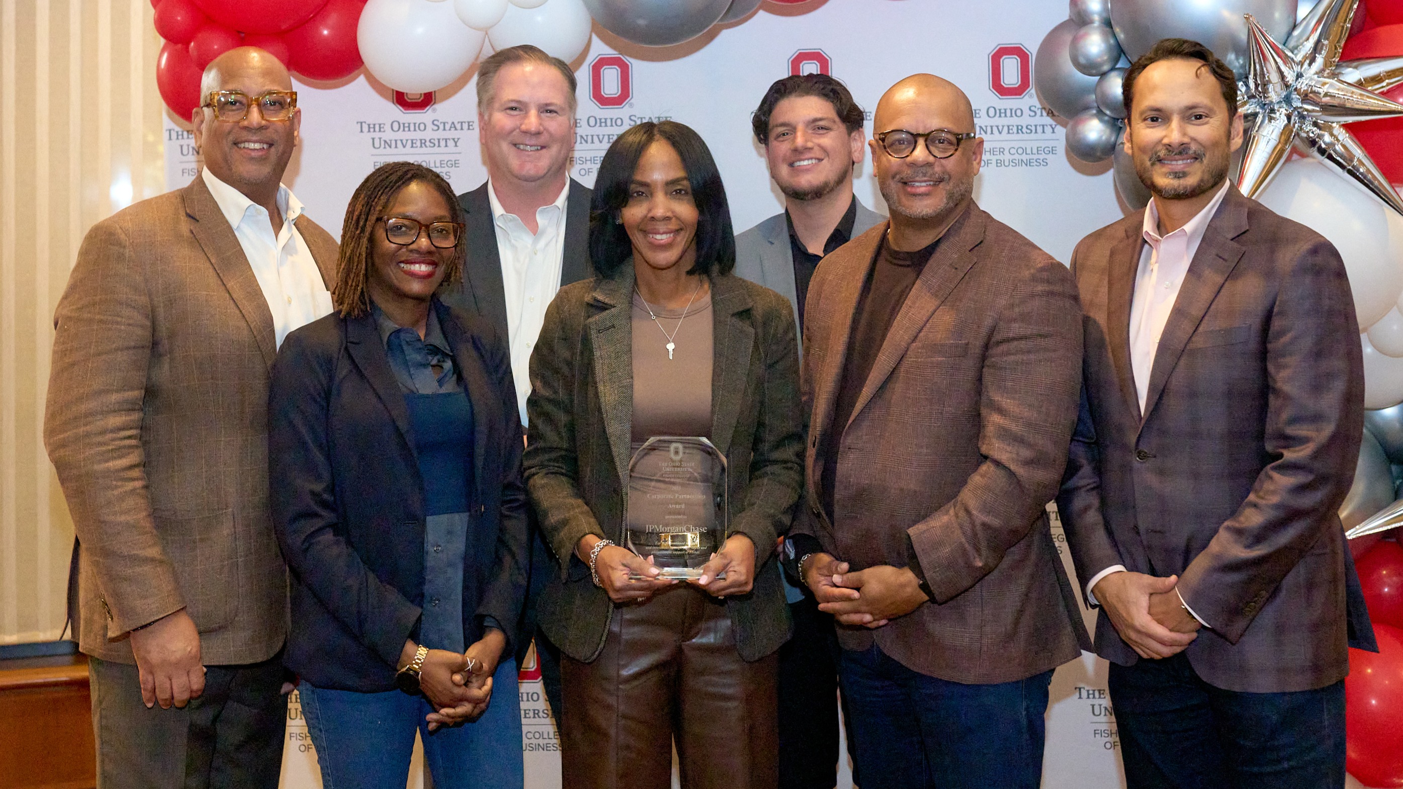 Employees of JPMorganChase pose with the Corporate Alumni Award in front of the Fisher College of Business sign and red, white and silver balloons.