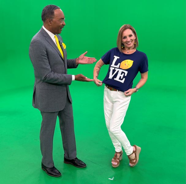 Man in suit with yellow tie points to woman in blue shirt with Love on it in front of a green background