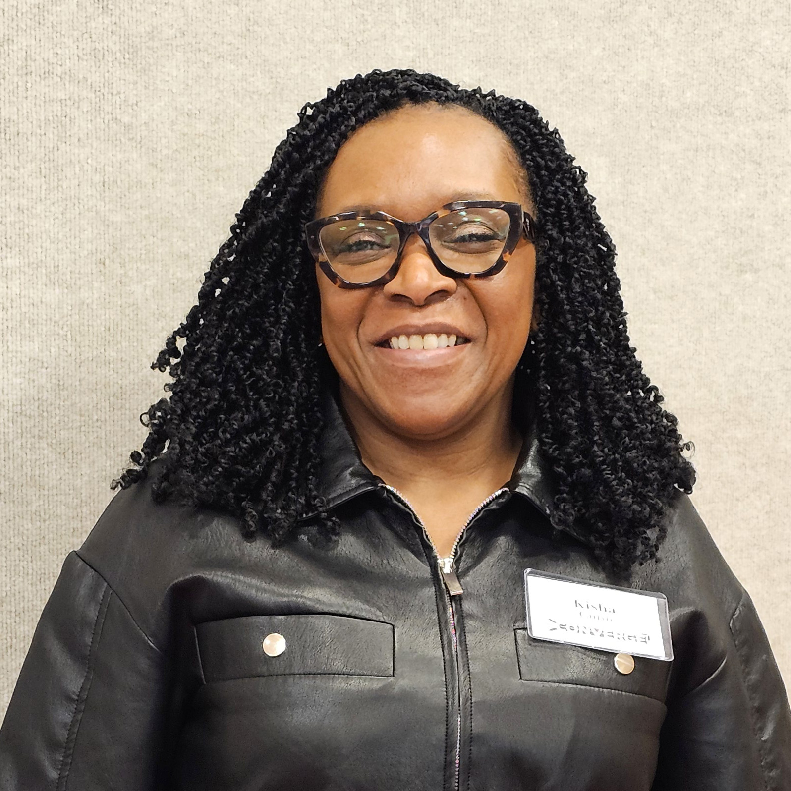 Kisha Gunn in a black jacket and tortoise shell glasses.