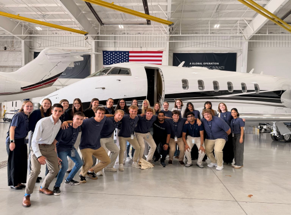 Group of people, arms around each other, in front of jet in a hangar