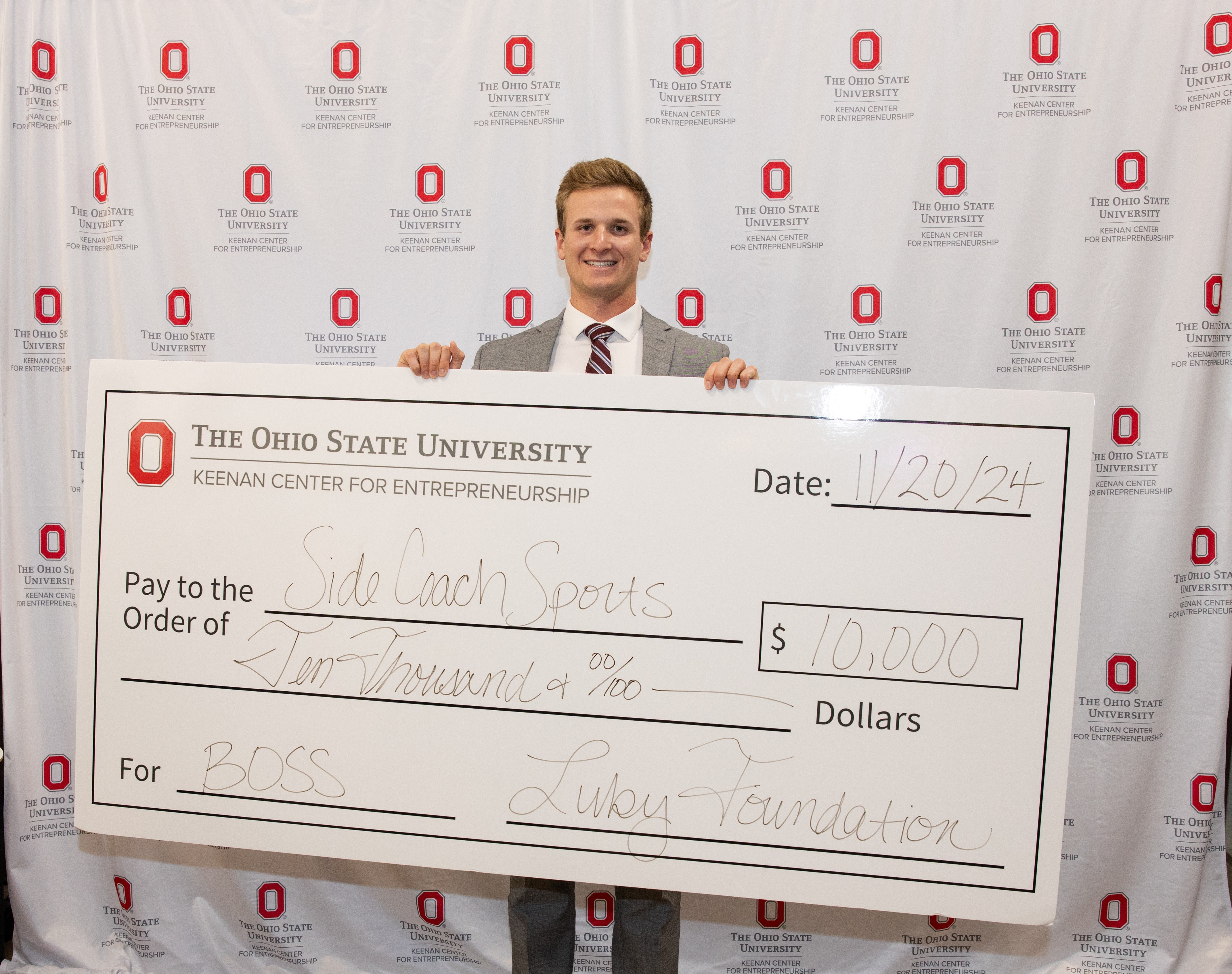 Luke Carrell displays large $10,000 check in front of backdrop covered with Ohio State logos