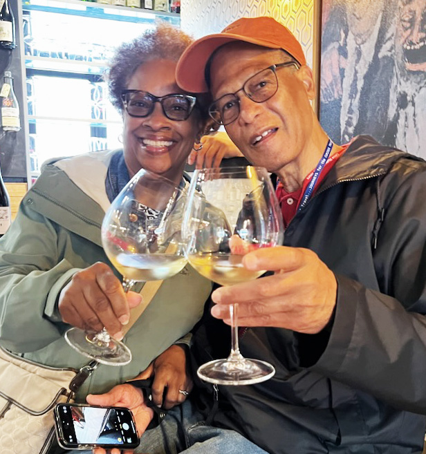Renee and Dwight Smith seated together in a bar toasting one another with a glass of wine.