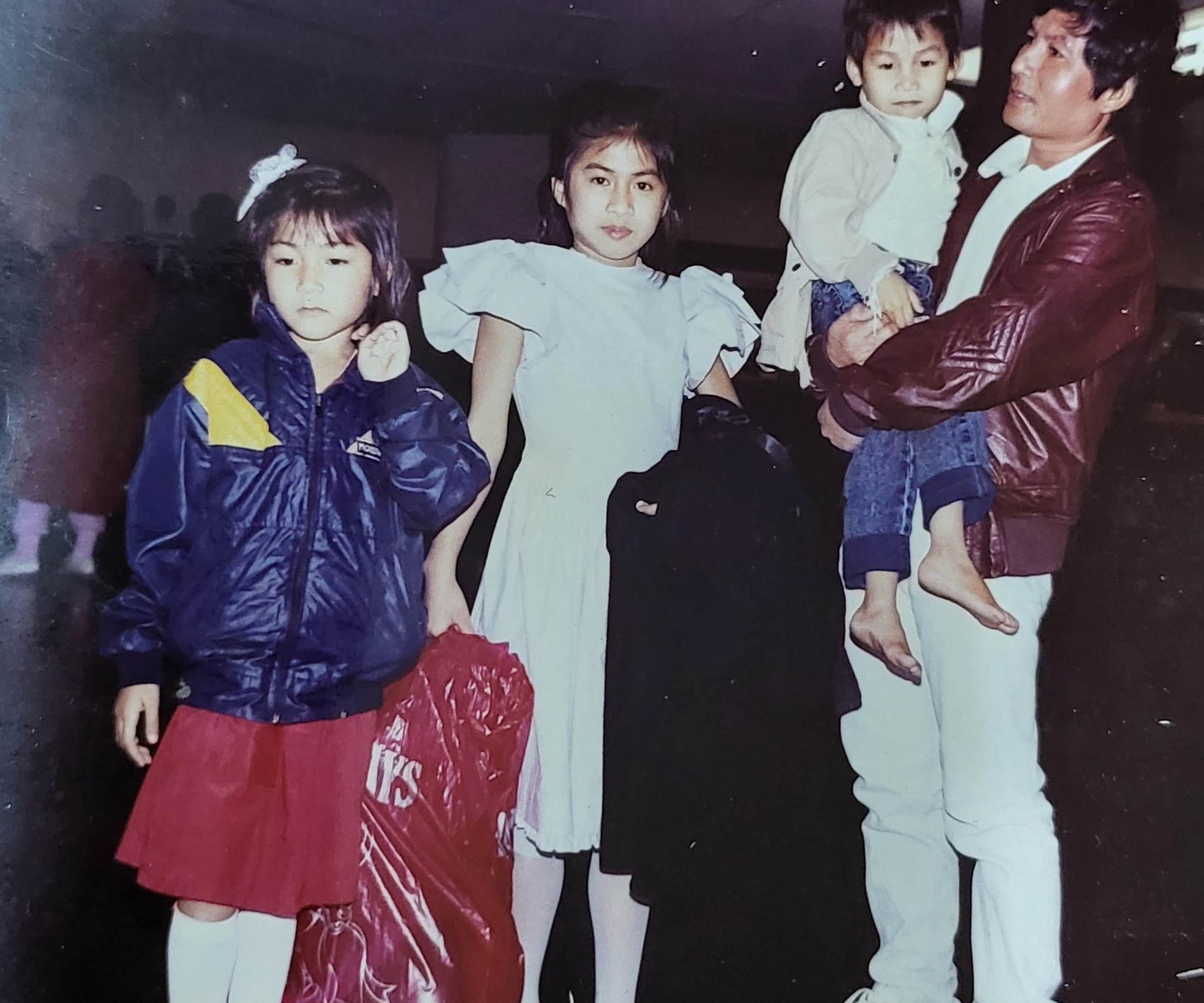 Sera, at left, with her older sister and younger brother in the arms of their father at the airport.