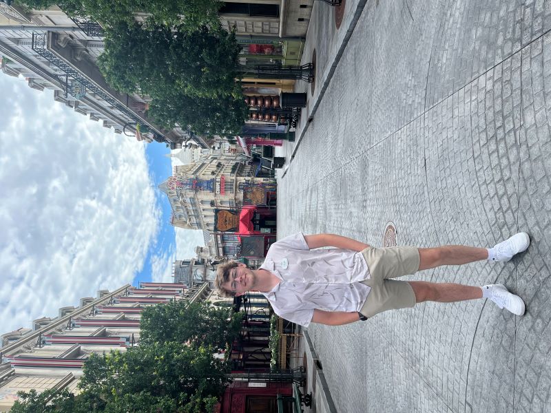 Tyler DiFranco stands on the street of The Wizarding World of Harry Potter: Ministry of Magic with buildings framing him