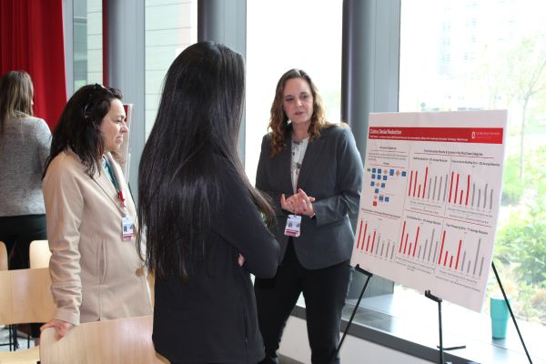 Three women standing around and looking at a poster board on an easel
