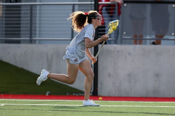 Woman in athletic top and shorts running down field holding a lacrosse stick