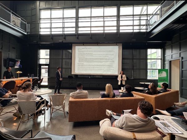 Large open area space with windows and employees sitting on couches while Amani and partner describe PowerPoint on screen