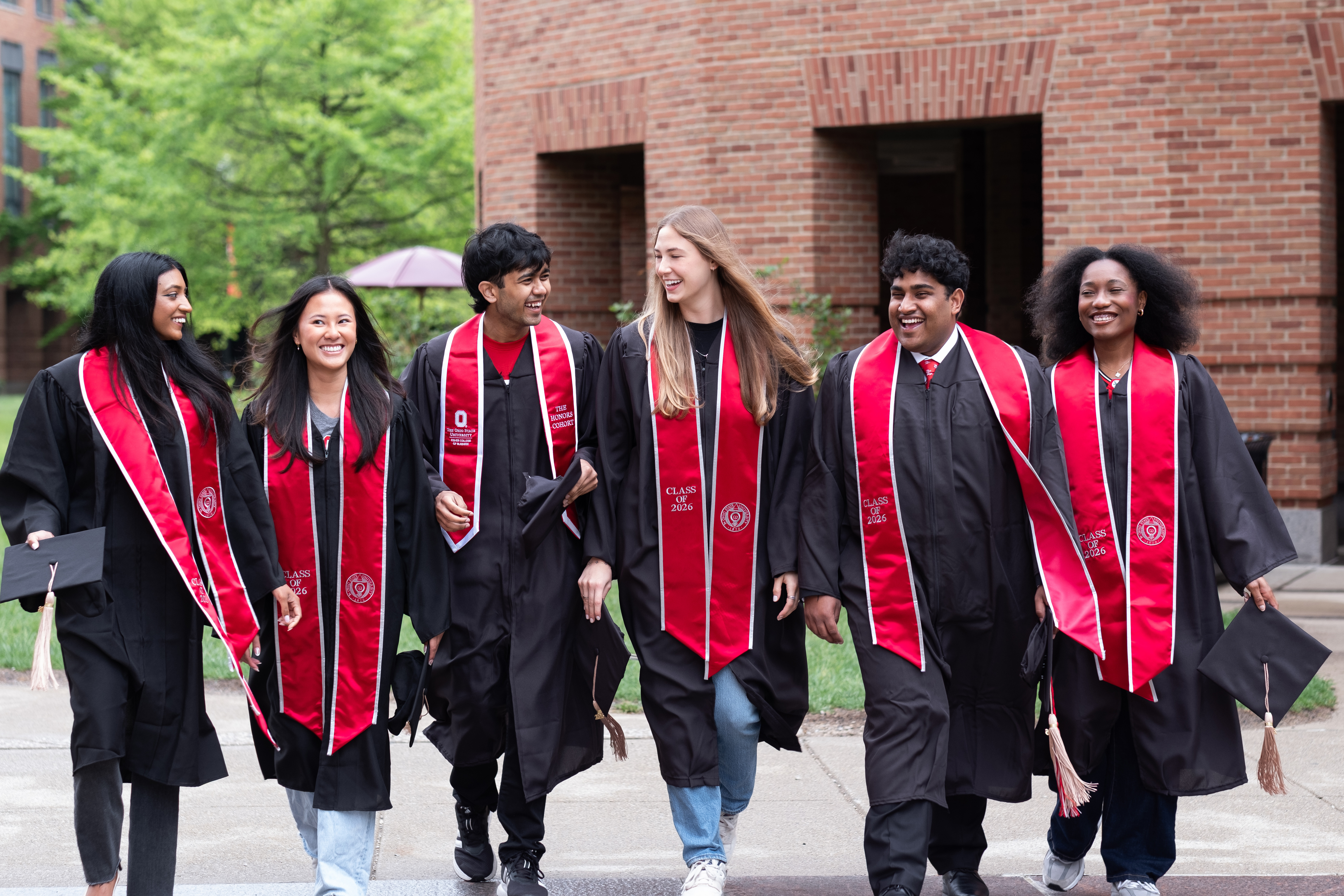 Students in their graduation regalia walking across the Fisher campus and smiling.