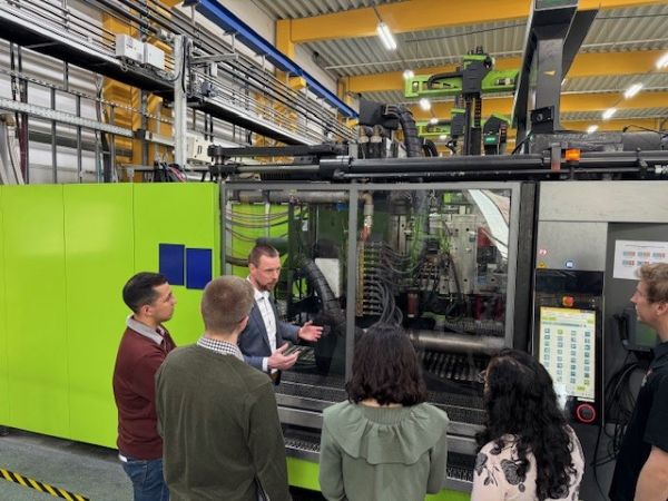 Students facing a manufacturing machine while and employee describes the process