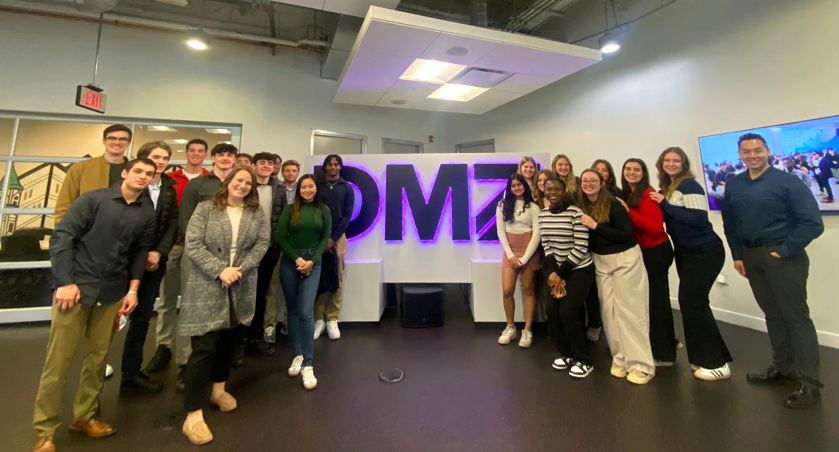 Group of students stand off to sides of neon DMZ sign in Toronto, Canada