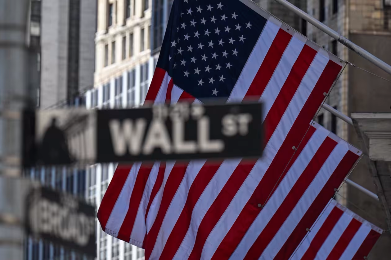 A Wall Street sign is displayed in front of American flags