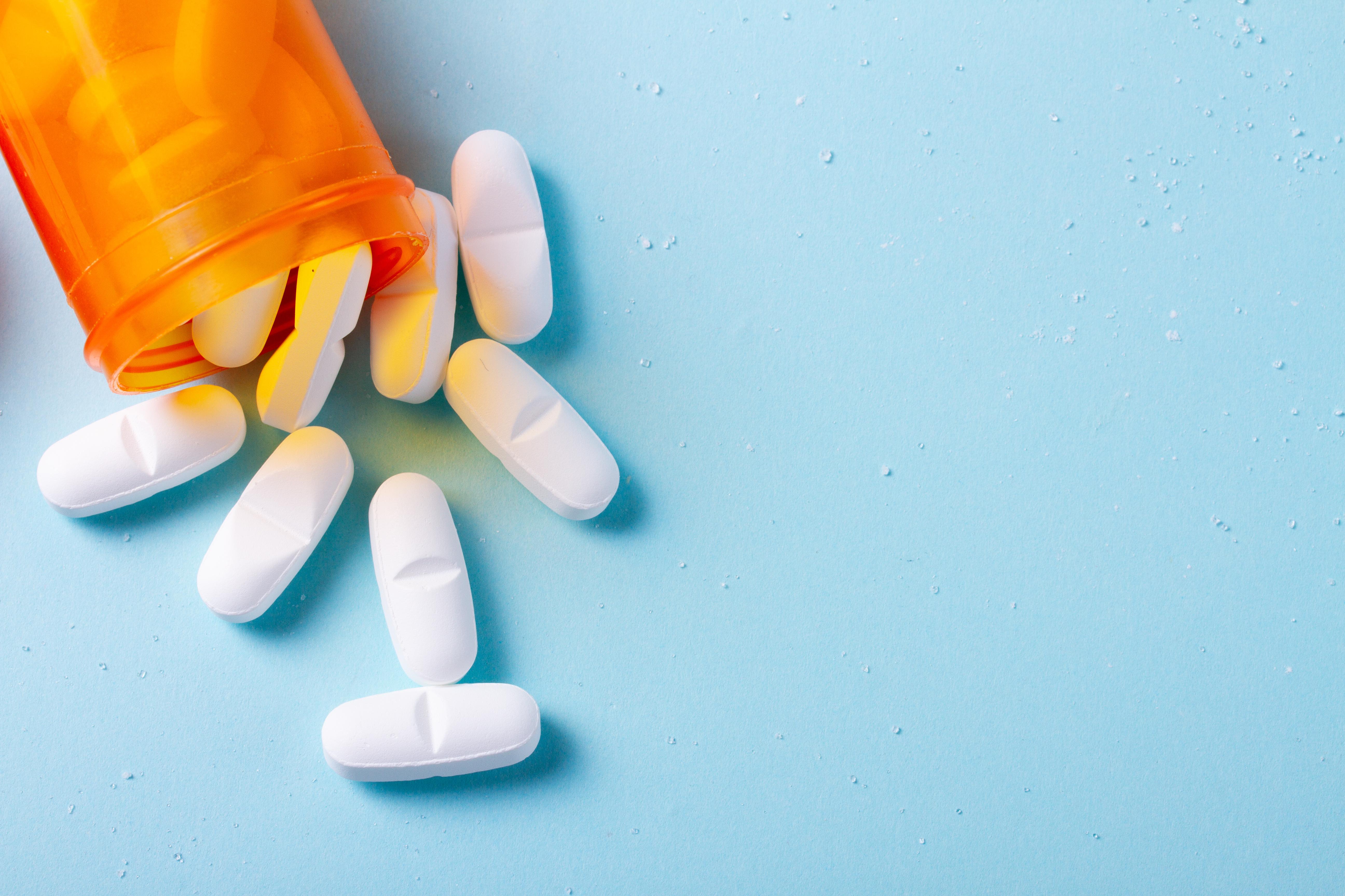 White pills spill from an orange pill bottle.