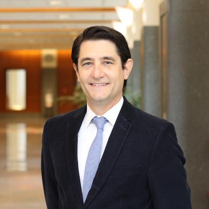 A headshot of Joe Goodman standing in a hallway in a suit and tie.