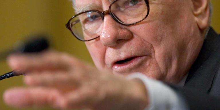 Warren Buffett gestures at a microphone.