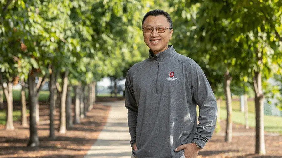 Daneil Leung poses in a gray Ohio State shirt on a path surrounded by trees.