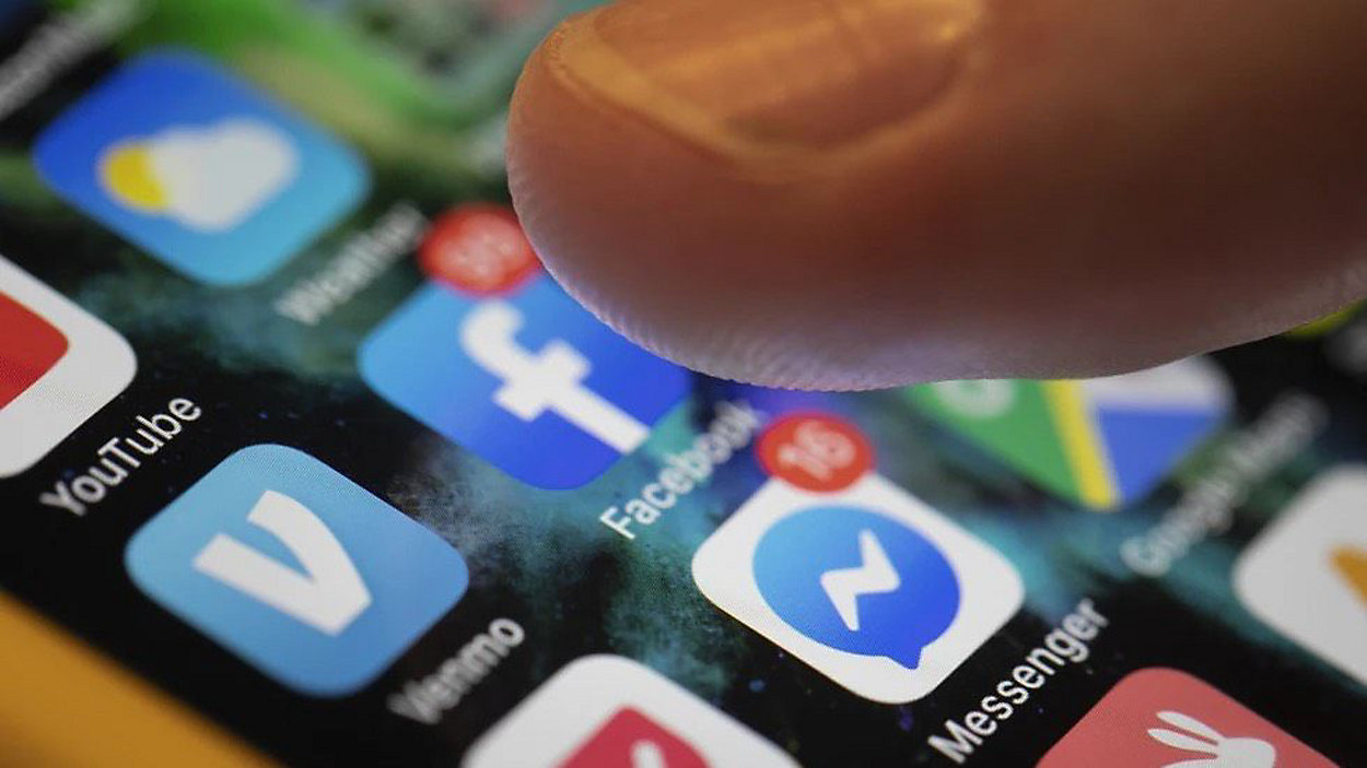 A finger hovers over a Facebook app on a phone.