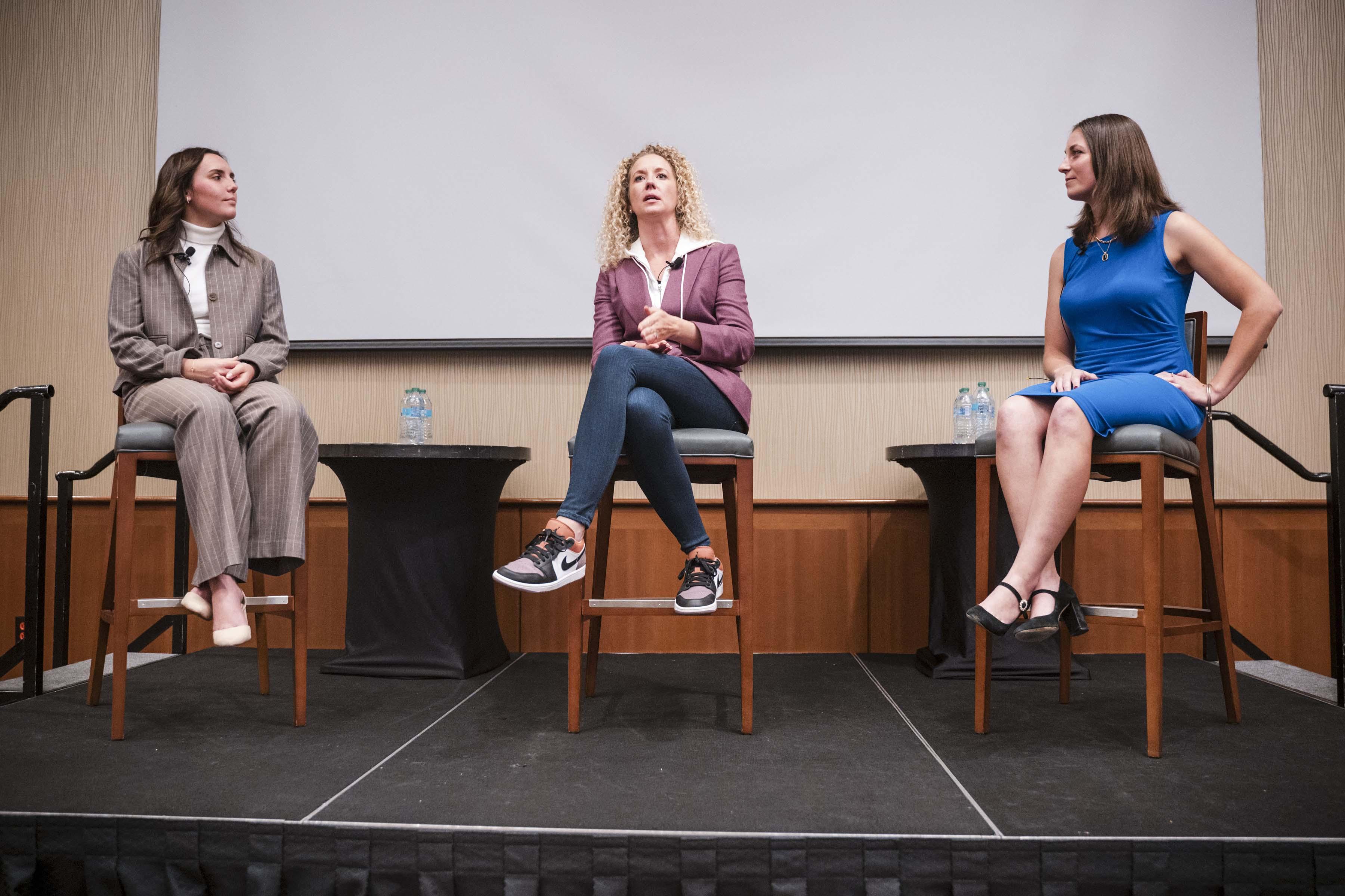 Becky Griffin seated on stage with students Marlie Moner and Chantel Fucci