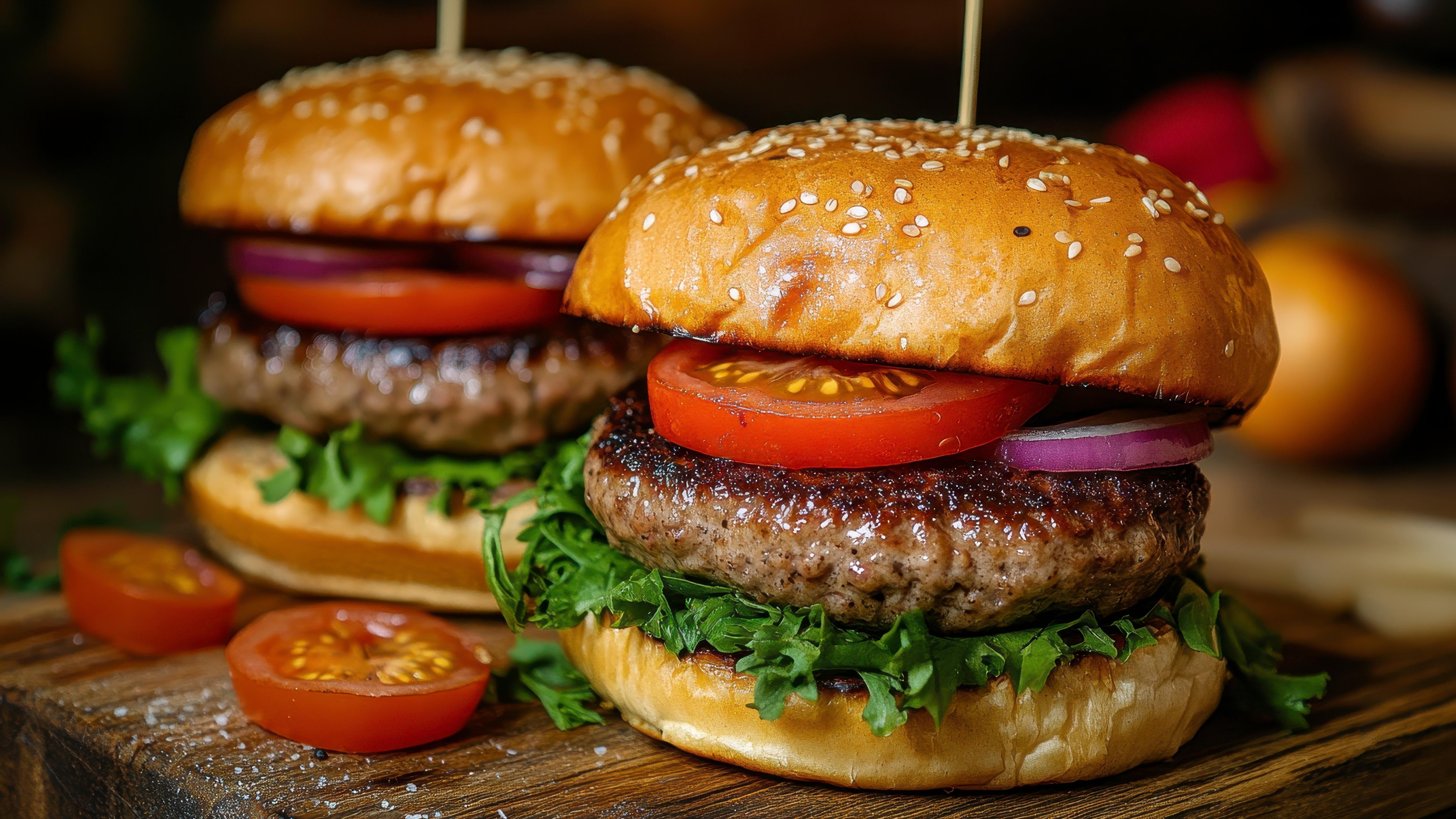 Two hamburgers with lettuce and tomato on sesame seed buns.