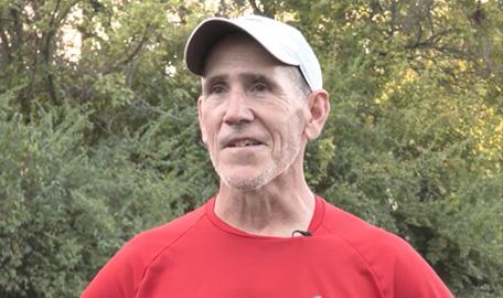 Steve Salopek answers questions wearing a red t-shirt and tan baseball cap.