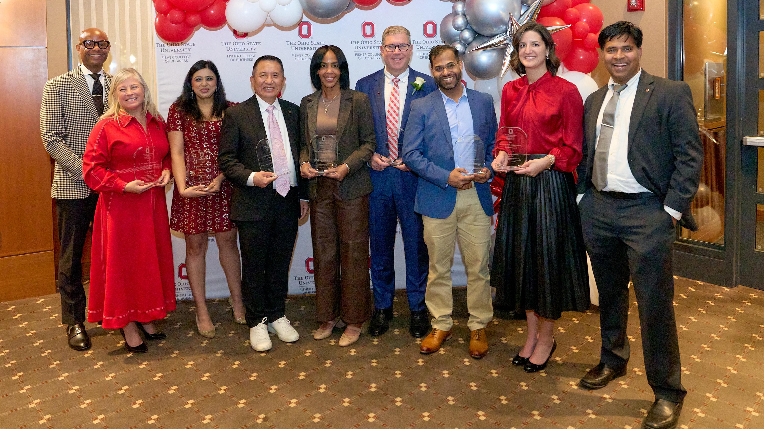 2025 Alumni Awards honorees pose with their awards in front of red, white and silver balloons.