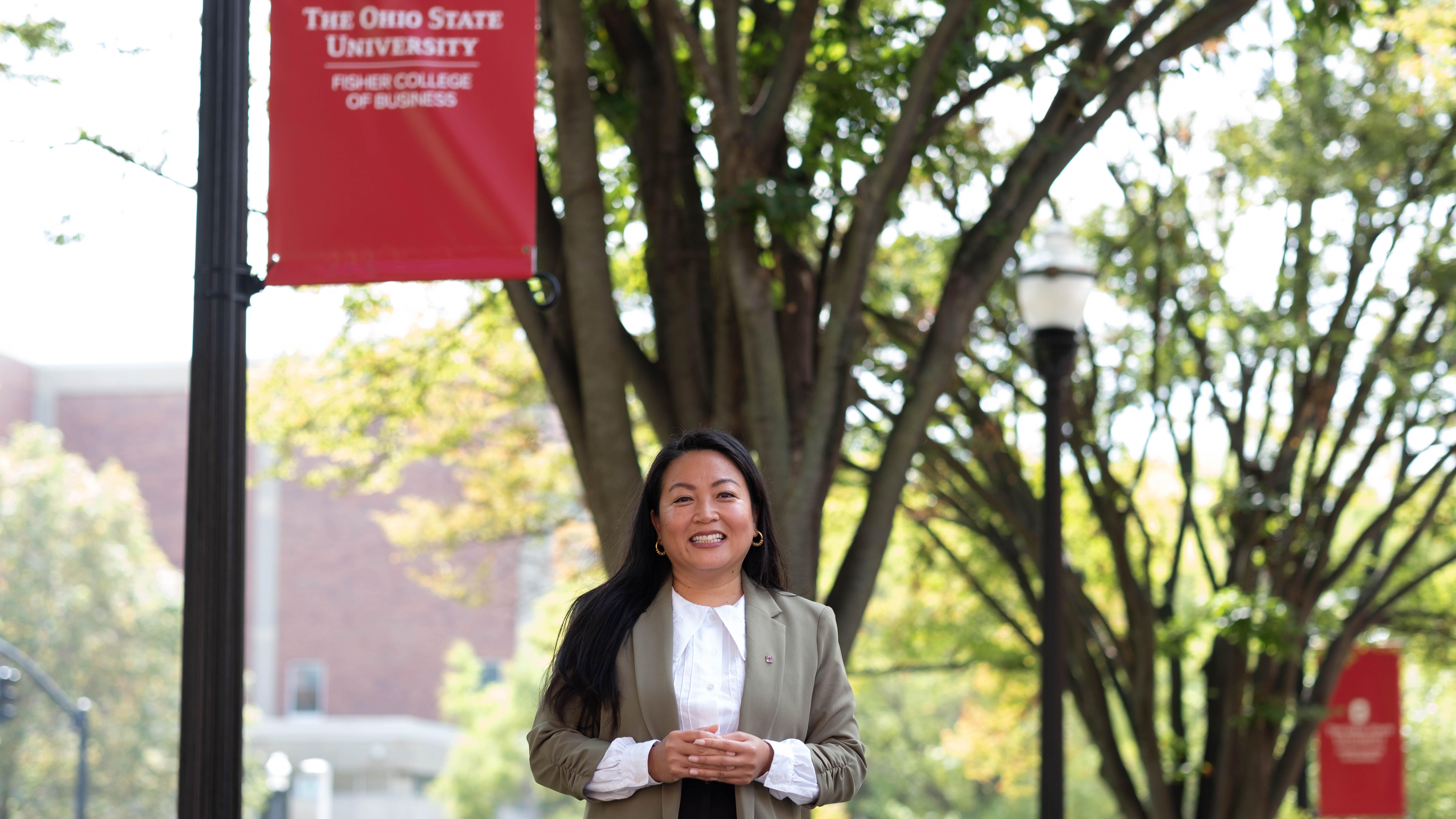 Sera Koulabdara stands outside on the Fisher campus beneath a red Ohio State Fisher College of Business banner