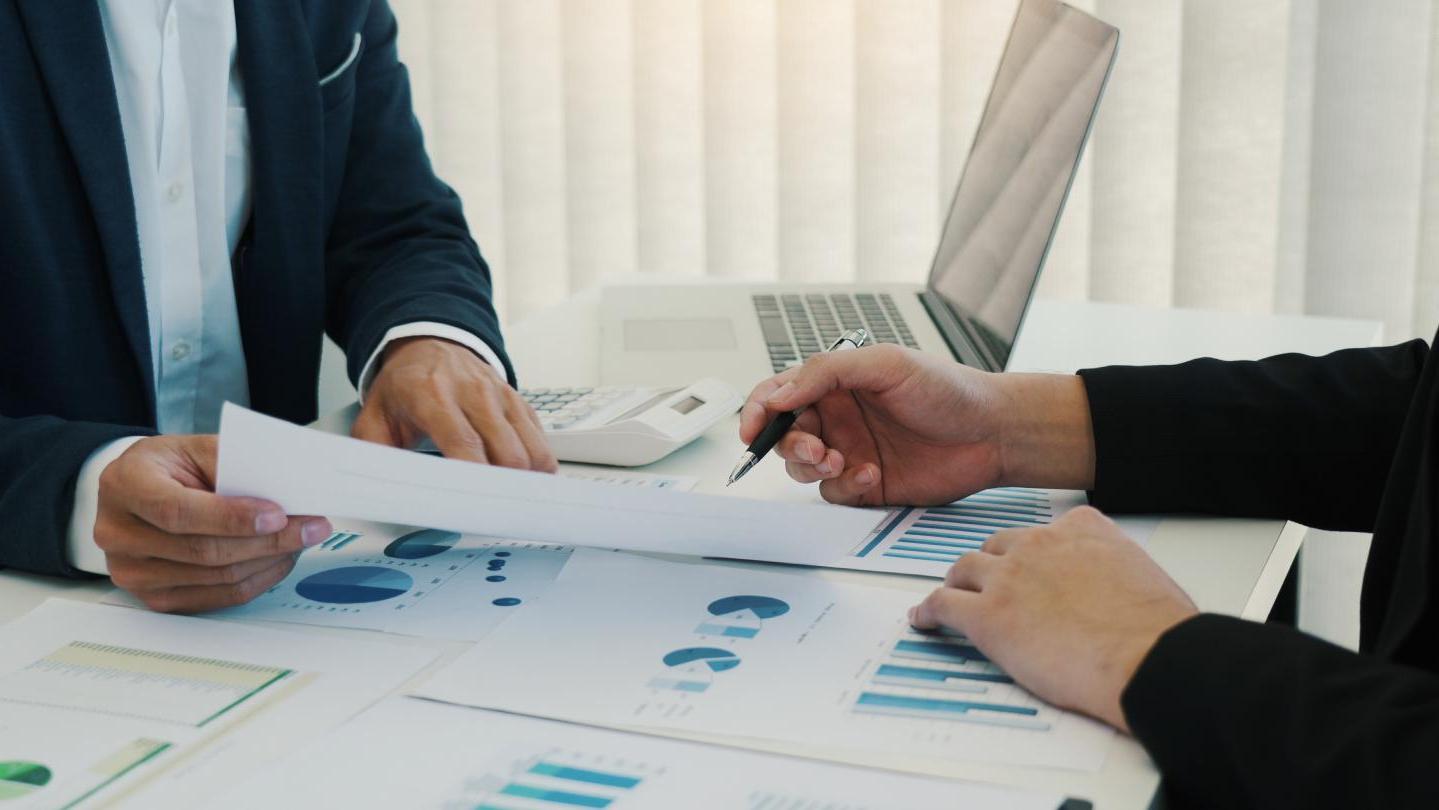 close up of two people working at a desk with a computer and paperwork