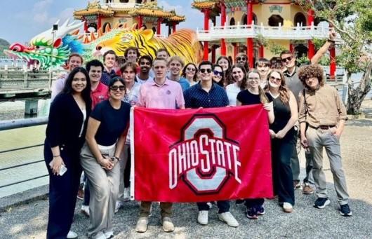 A group of students holding an Ohio State flag in front of pagodas.