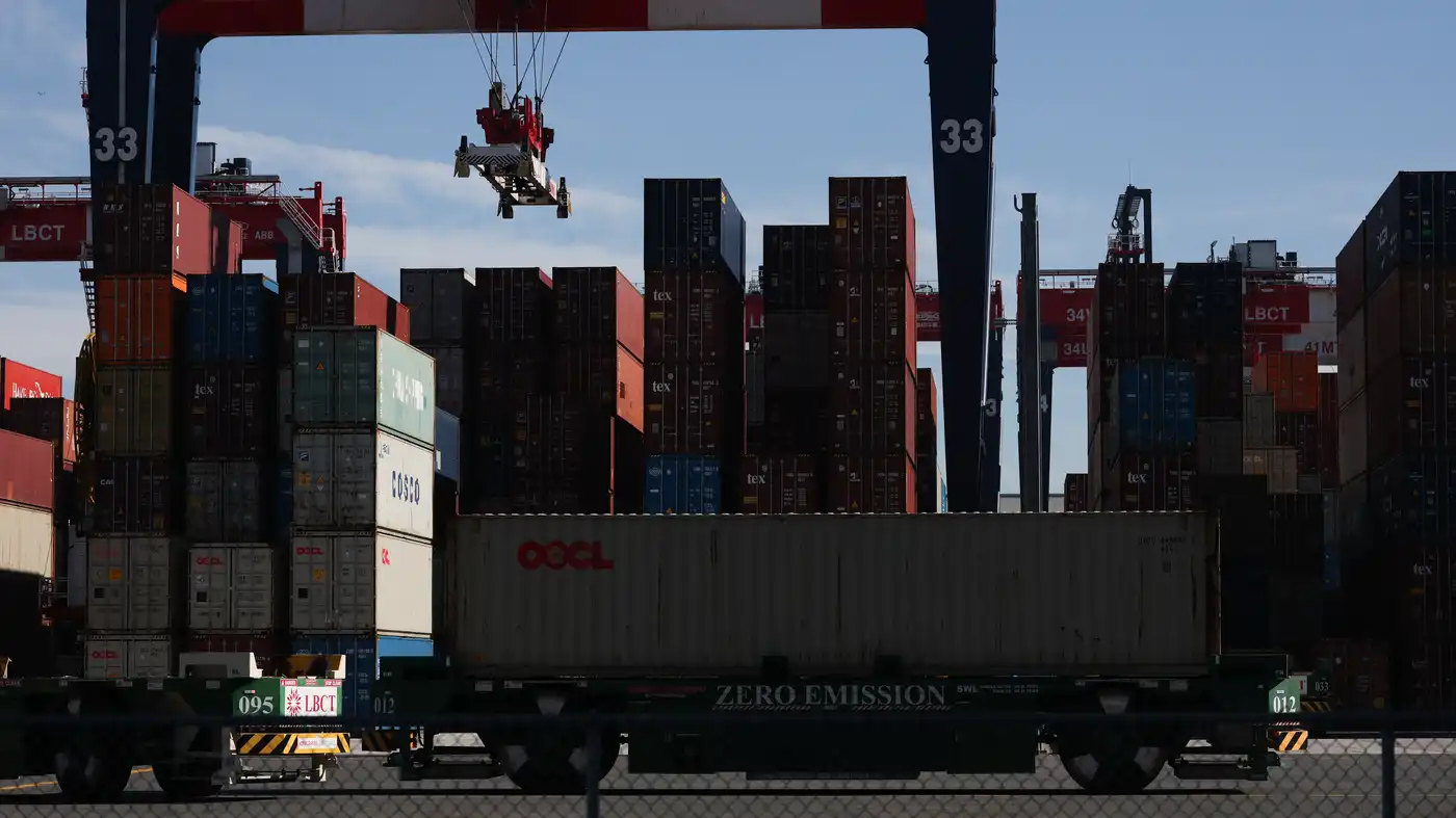 Shipping containers stacked at a busy port terminal as a crane lifts a container overhead above a zero-emission truck.