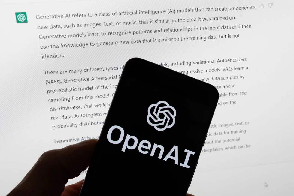 Hand holding a smartphone displaying the OpenAI logo, with blurred text about generative AI visible on a screen in the background.
