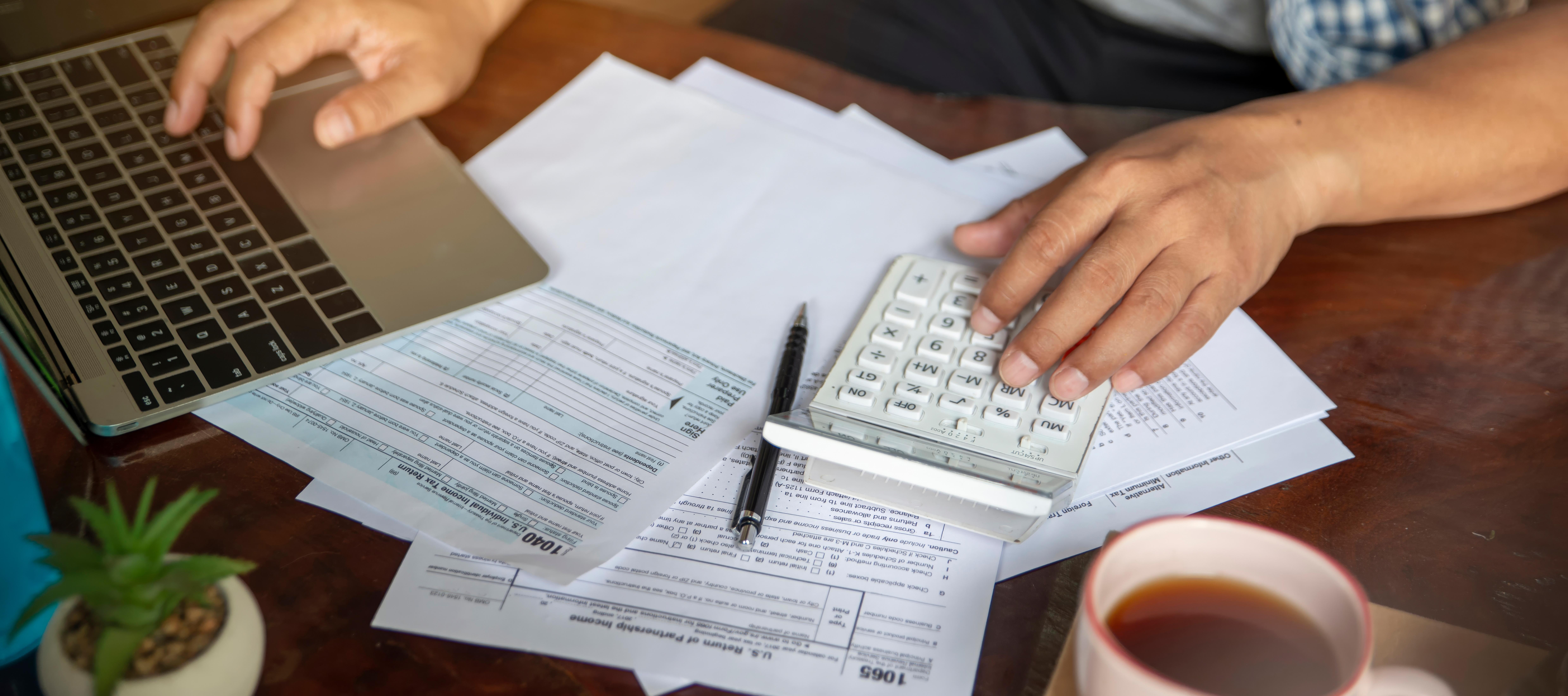A detail shot of someone preparing tax documents with an open laptop.
