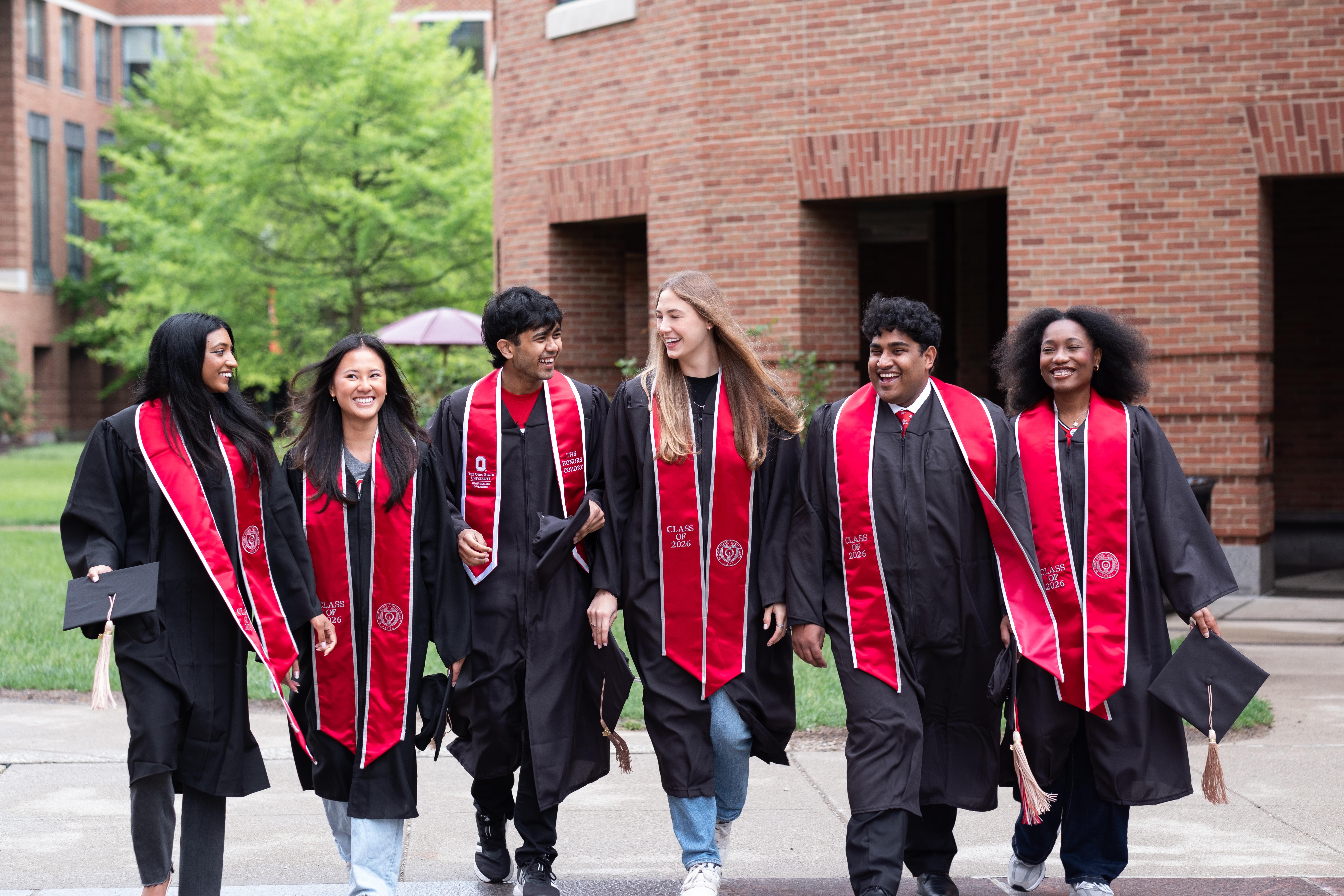 Group of students in graduation gowns walking across Fisher campus