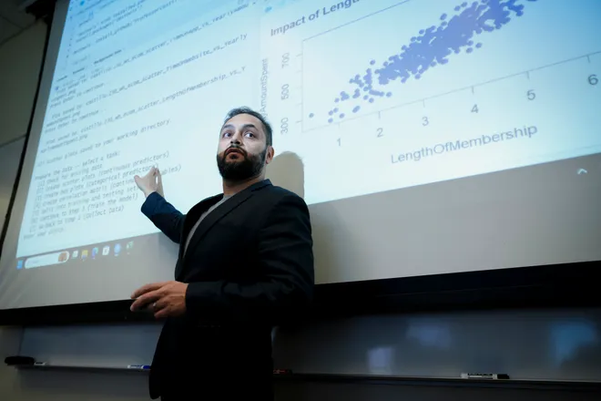 Vince Castillo, in a suit, gestures to a presentation slide.