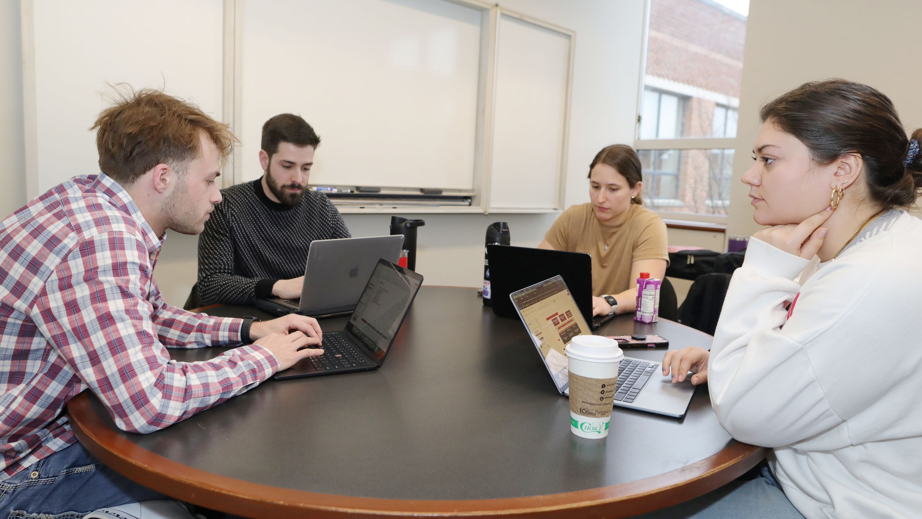MBA students huddle around laptops working on a project in a conference room.