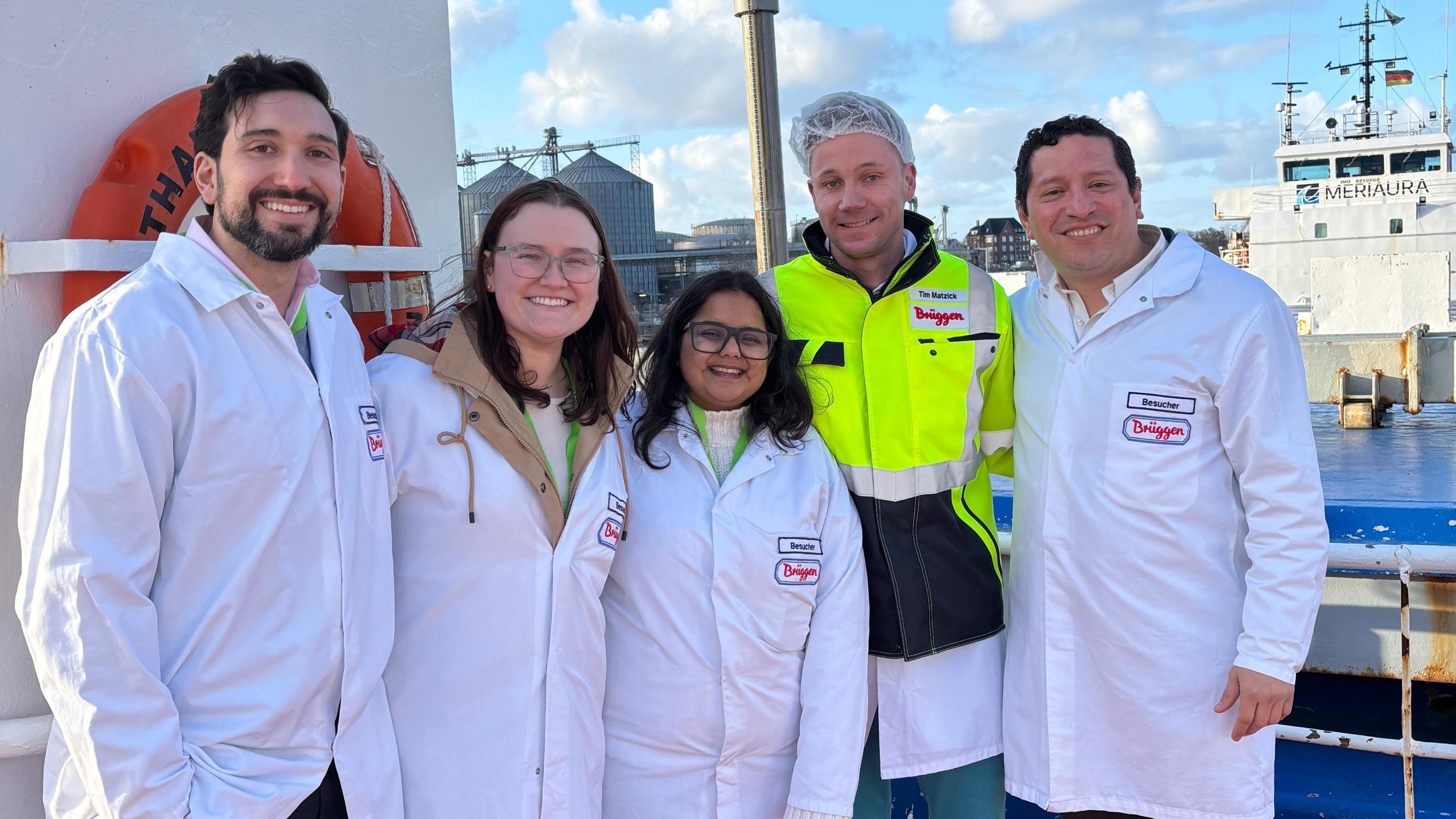 Group of MBA students in white lab coats posing on a ship deck during an industrial oat milling facility tour.