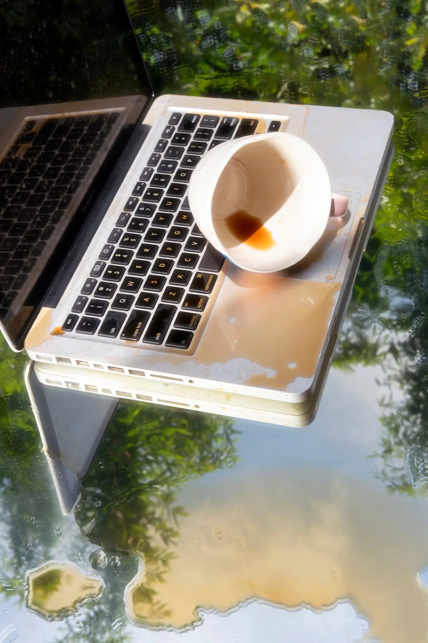 Spilled coffee cup resting on a laptop keyboard, with coffee spread across the computer.